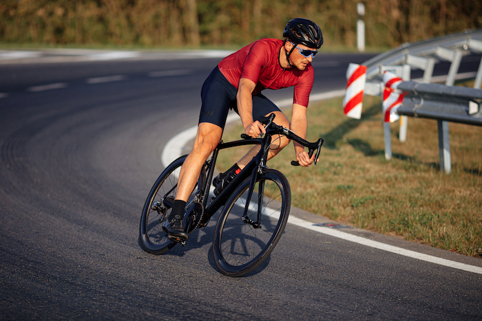 Male athlete dressed in sport clothing, mirrored eyewear and protective helmet using black bike for riding on asphalt road. Sport activity outdoors.